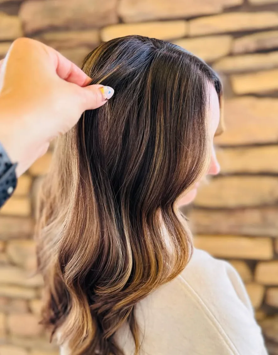 Glossy brunette balayage with warm ribbons and softly curled ends